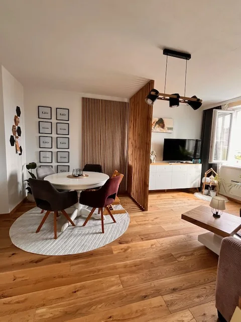 Wohnzimmer mit rundem Esstisch und Raumteiler aus Eichenlamellen vor dem Fernsehbereich, Kundenfoto